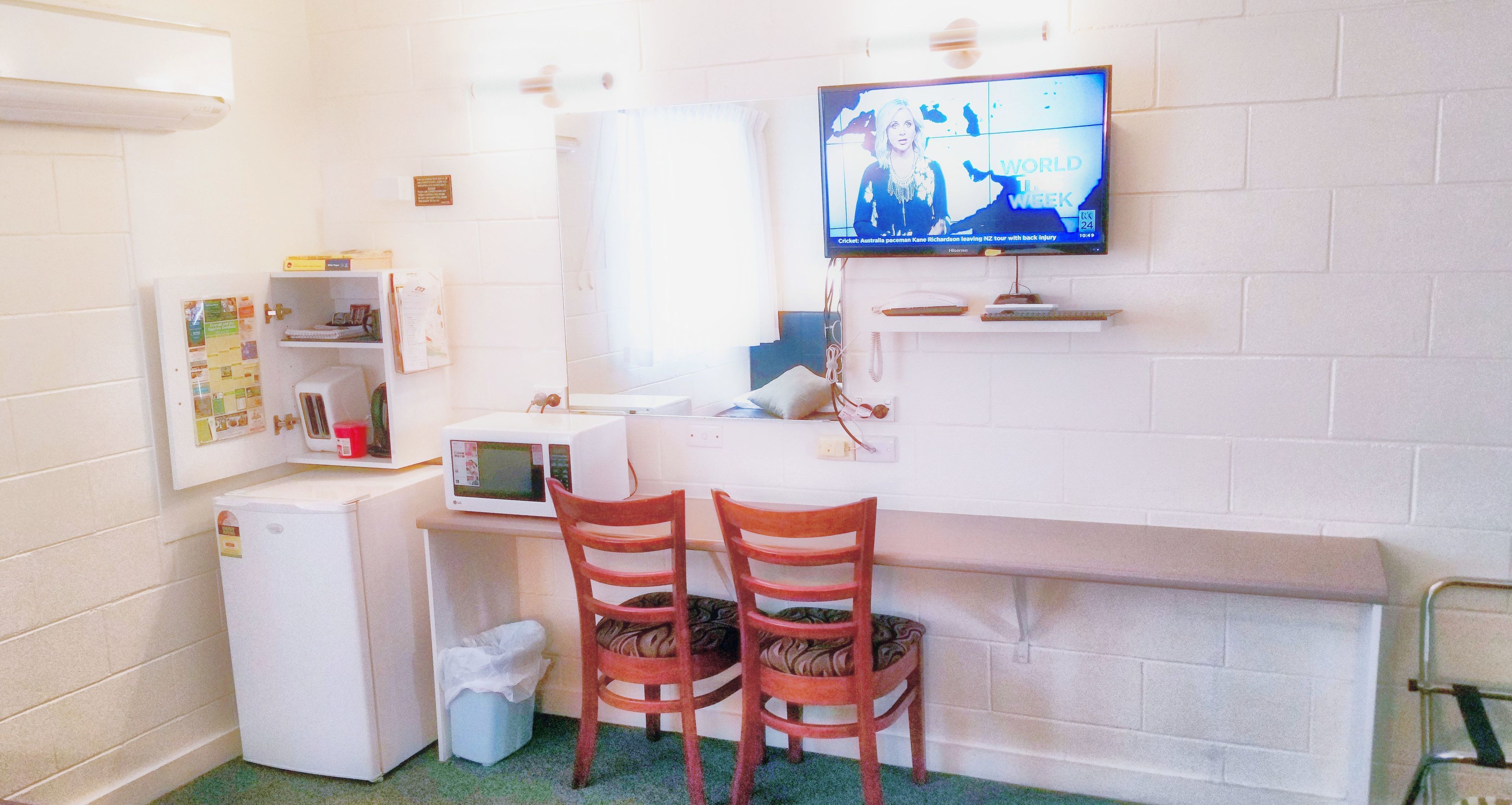 A compact kitchenette with a microwave, a small fridge, a sink, and two wooden chairs.
