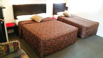 A room with two beds, each with patterned bedspreads and pillows, a small table with a red mat, and a colorful chair.