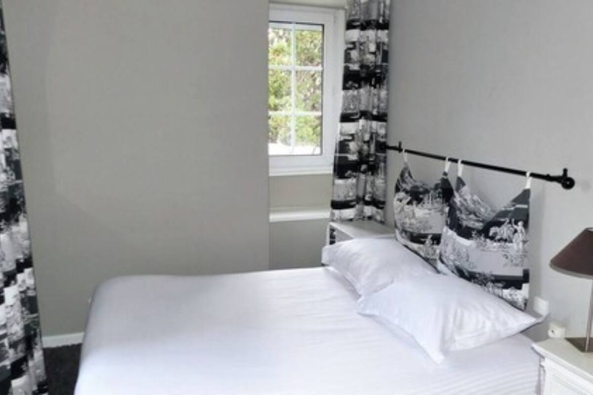 A bedroom with a bed, a window, a lamp, and a curtain with a mountain design.