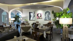 A restaurant with round tables, chairs, and a large potted plant. - LE H - Hôtel & Restaurant (Barr)