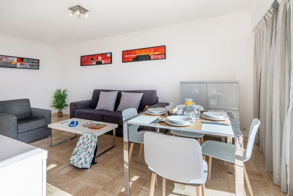 A modern living room with a sofa, dining table, chairs, and artwork on the walls. - Nemea Appart Hotel Le Lido Cagnes sur Mer (Cagnes-sur-Mer)