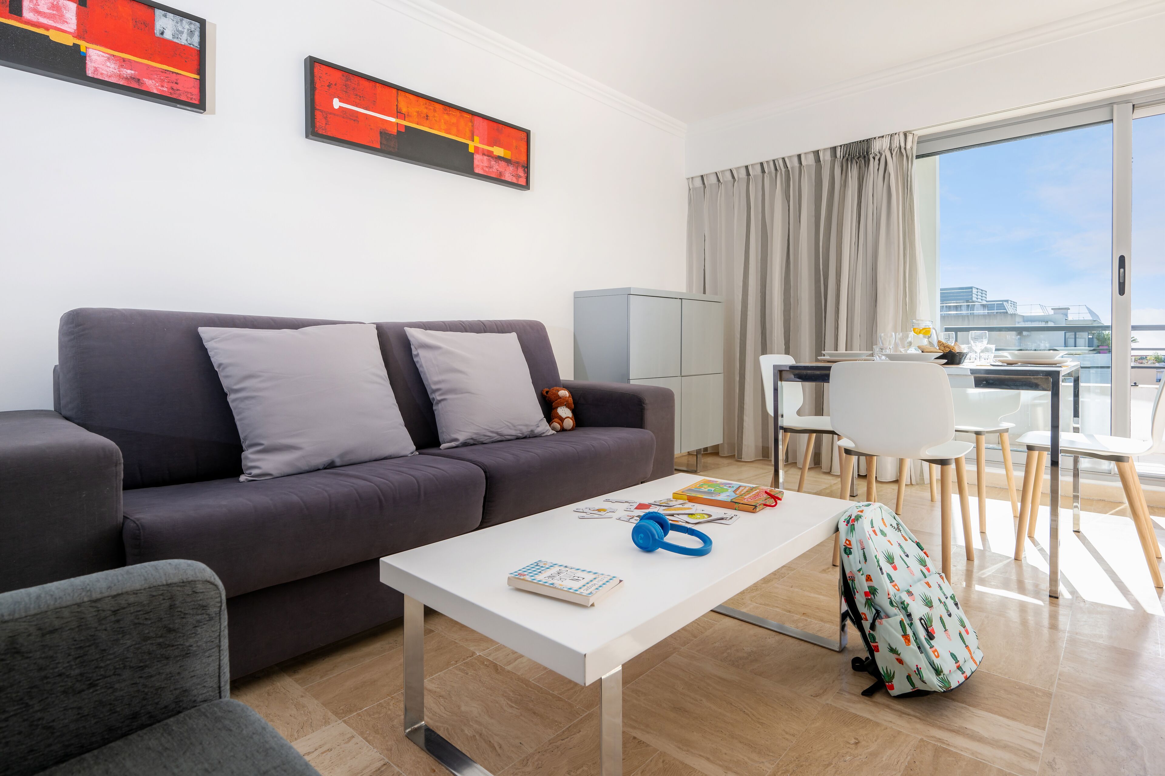 A modern living room with a grey sofa, a white coffee table, and a dining area with a table and chairs.