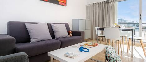 A modern living room with a grey sofa, a white coffee table, and a dining area with a table and chairs.