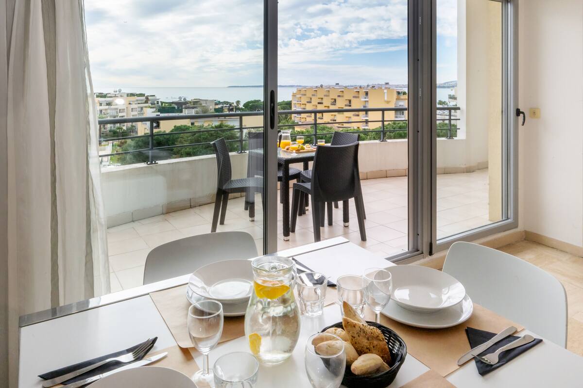 A balcony with a table set for breakfast, including plates, glasses, and a pitcher of water.