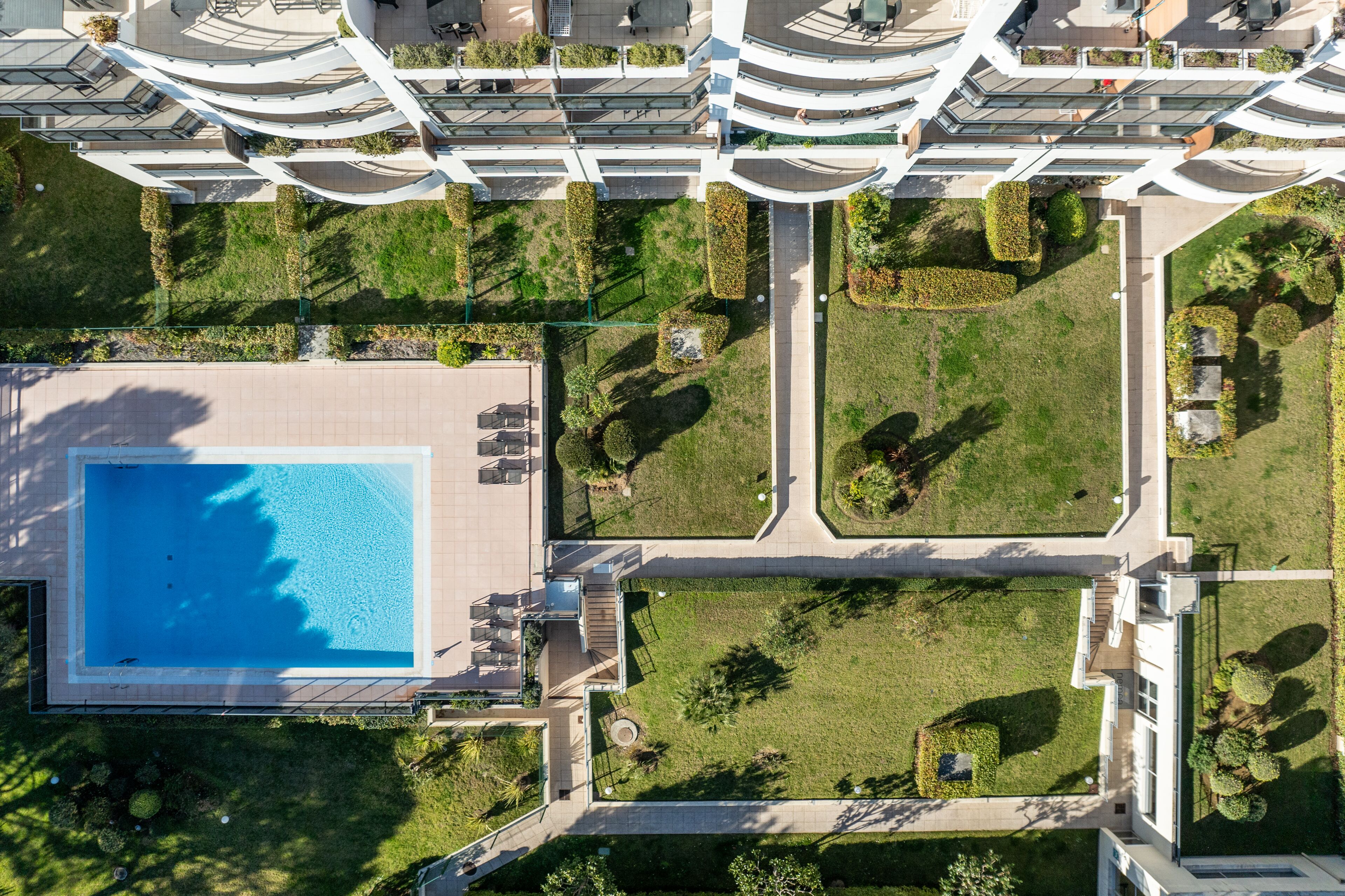 An aerial view of a modern building with a swimming pool, landscaped gardens, and multiple balconies.