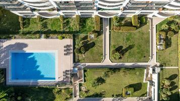 An aerial view of a modern building with a swimming pool, landscaped gardens, and multiple balconies.