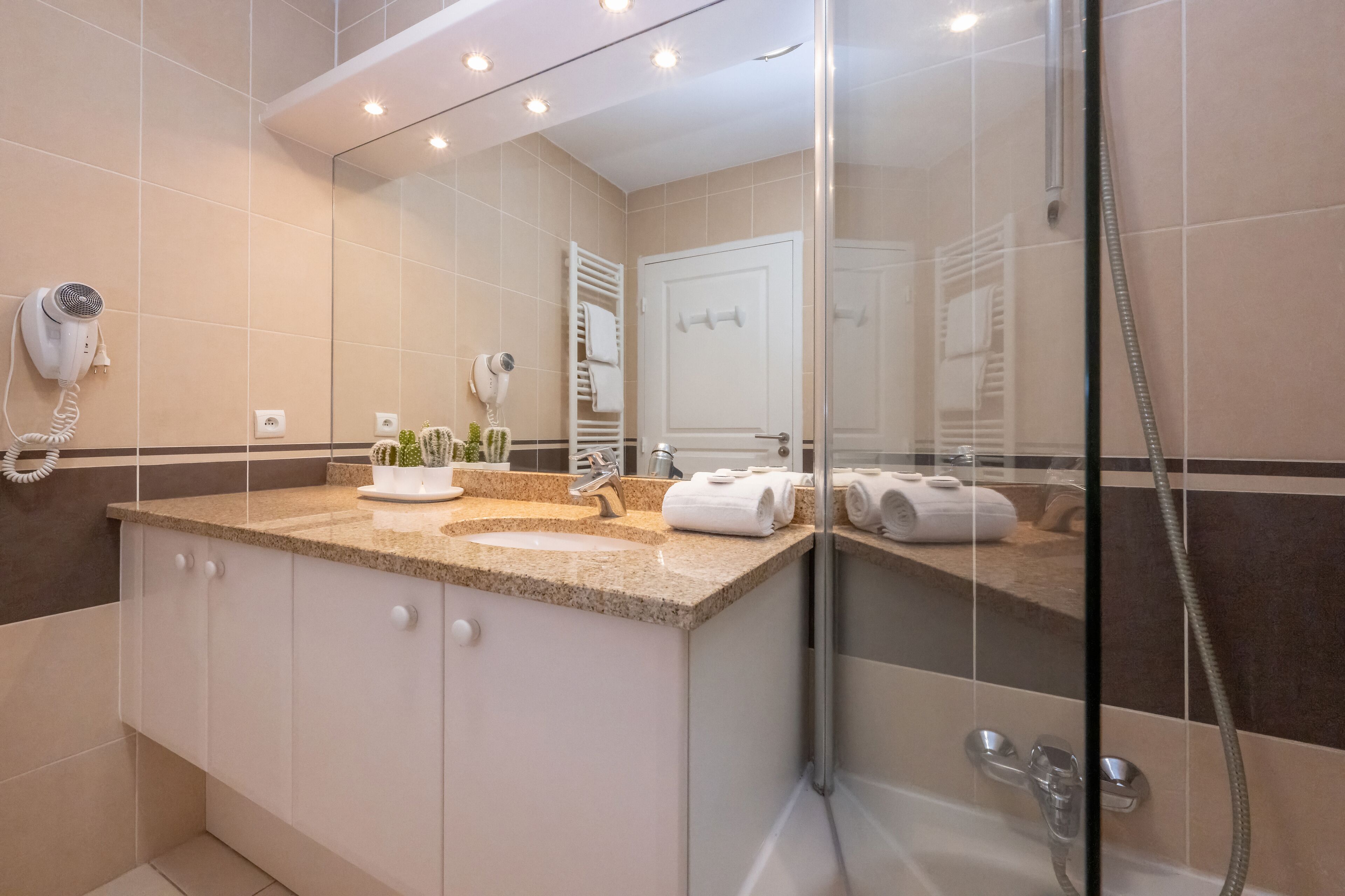 A modern bathroom with a glass shower enclosure, a vanity with a sink, and a hairdryer mounted on the wall.