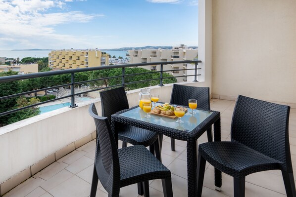 A balcony with a table set for breakfast, overlooking a cityscape and a body of water.