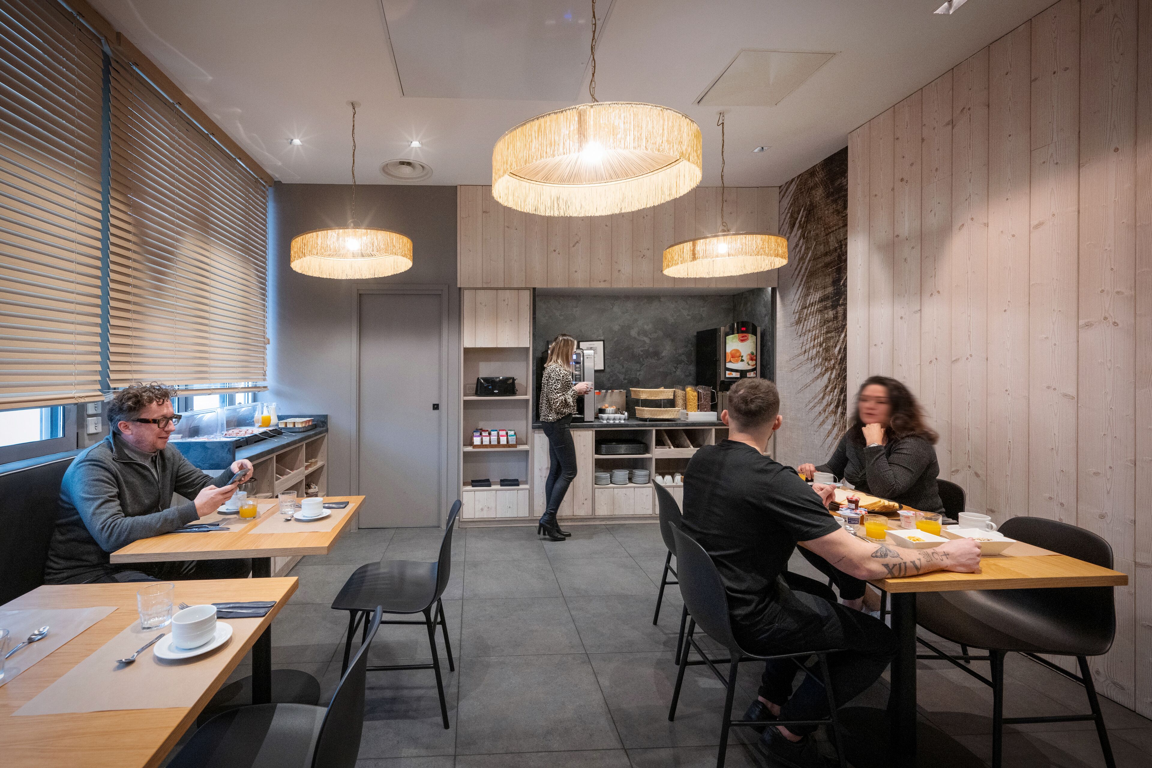 A modern dining area with wooden walls, pendant lighting, and a visible kitchen area in the background.