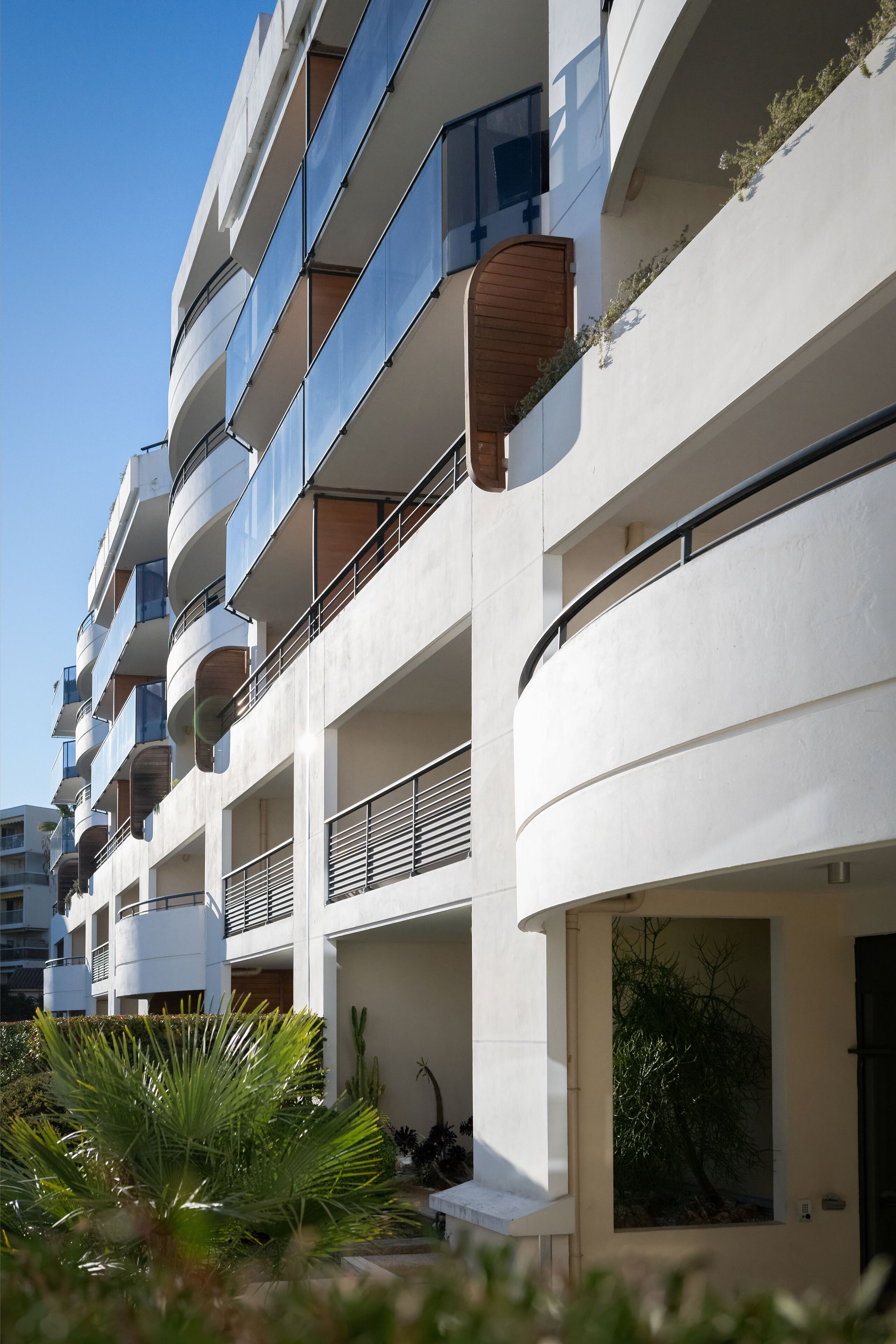 Un edificio de varios pisos con balcones, fachada plana y un pequeño jardín al frente.