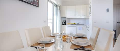 A dining area with a table set for six, white chairs, and a kitchen in the background.