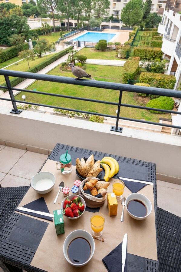 Un balcon avec des éléments pour le petit-déjeuner, un oiseau et une vue sur une piscine.