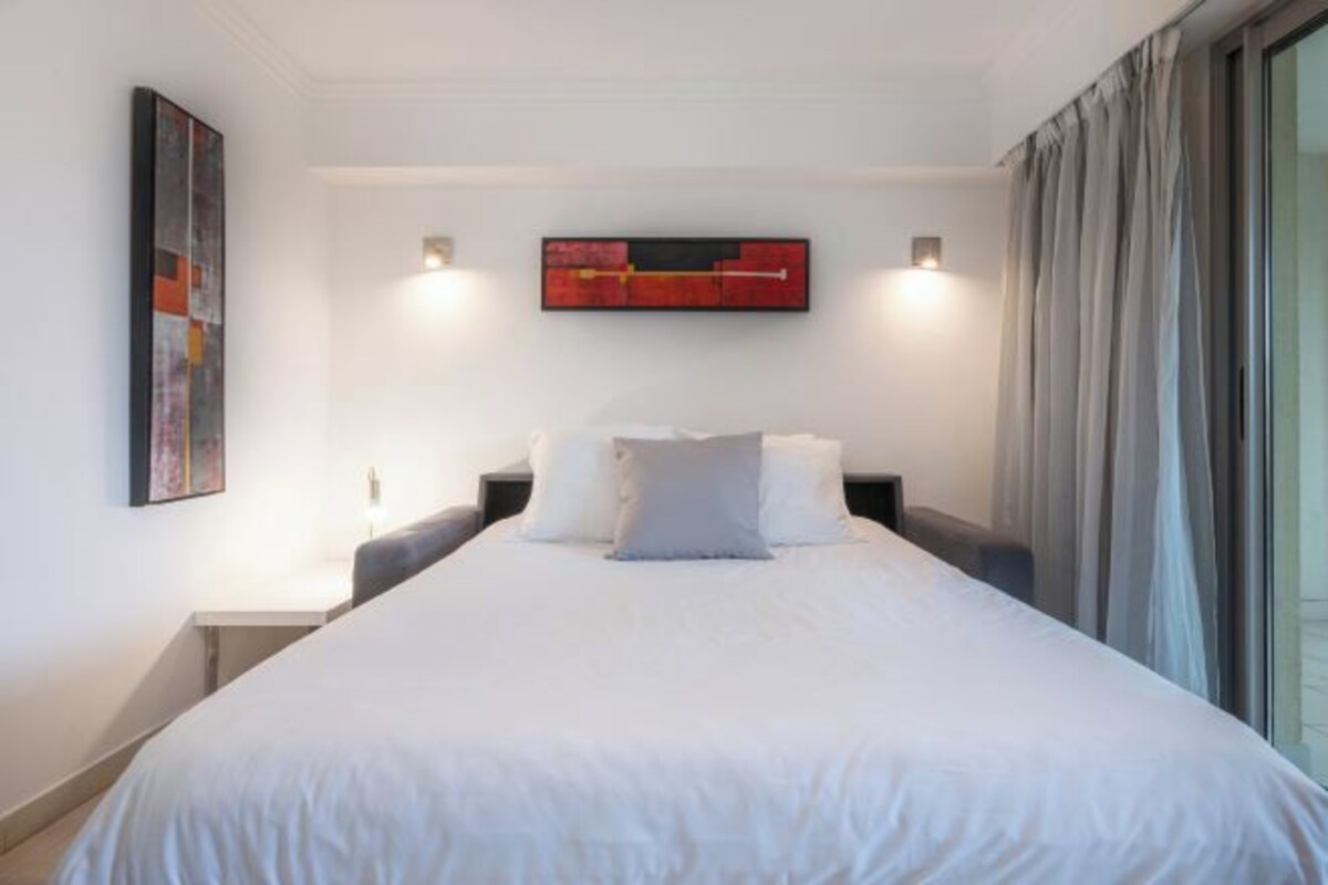 A hotel room with a large bed, a nightstand, a wall-mounted artwork, and a window with curtains.