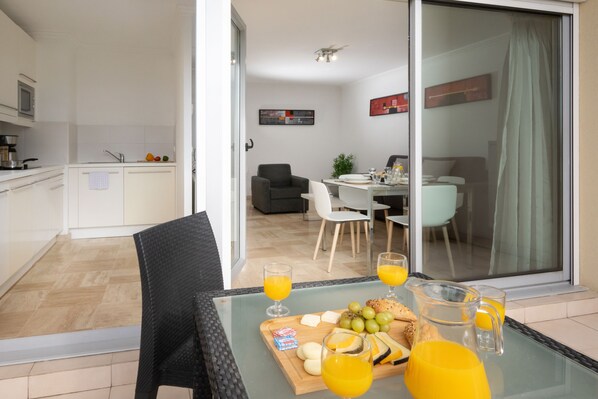 Una cocina moderna con armarios blancos, un comedor con mesa de vidrio y vistas a una sala de estar a través de un cerramiento corredizo.