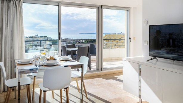 A modern dining area with a balcony view, a flat-screen TV, and a minimalist design. - Nemea Appart Hotel Le Lido Cagnes sur Mer (Cagnes-sur-Mer)