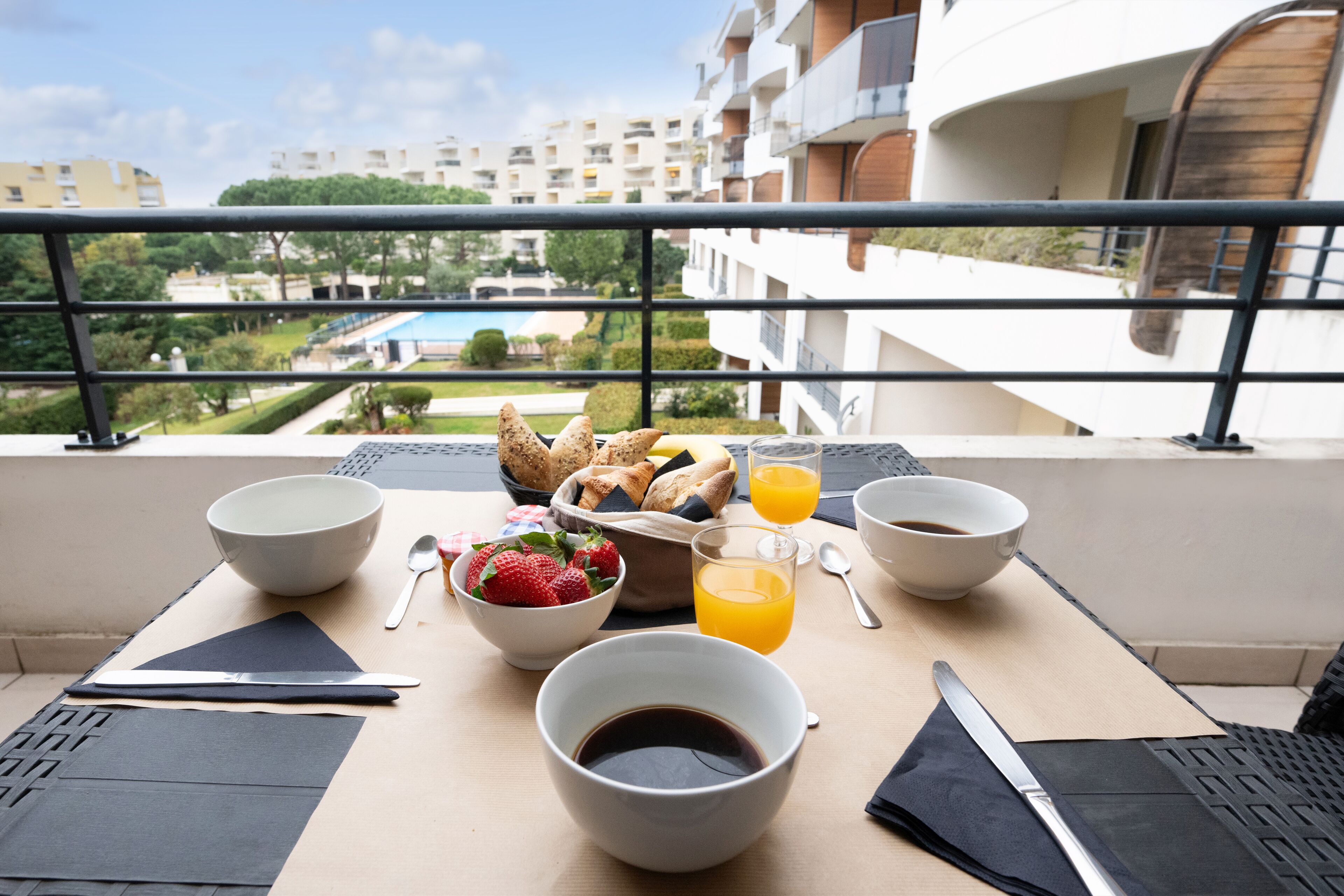 A breakfast setup on a balcony with a view of a pool and apartment buildings.