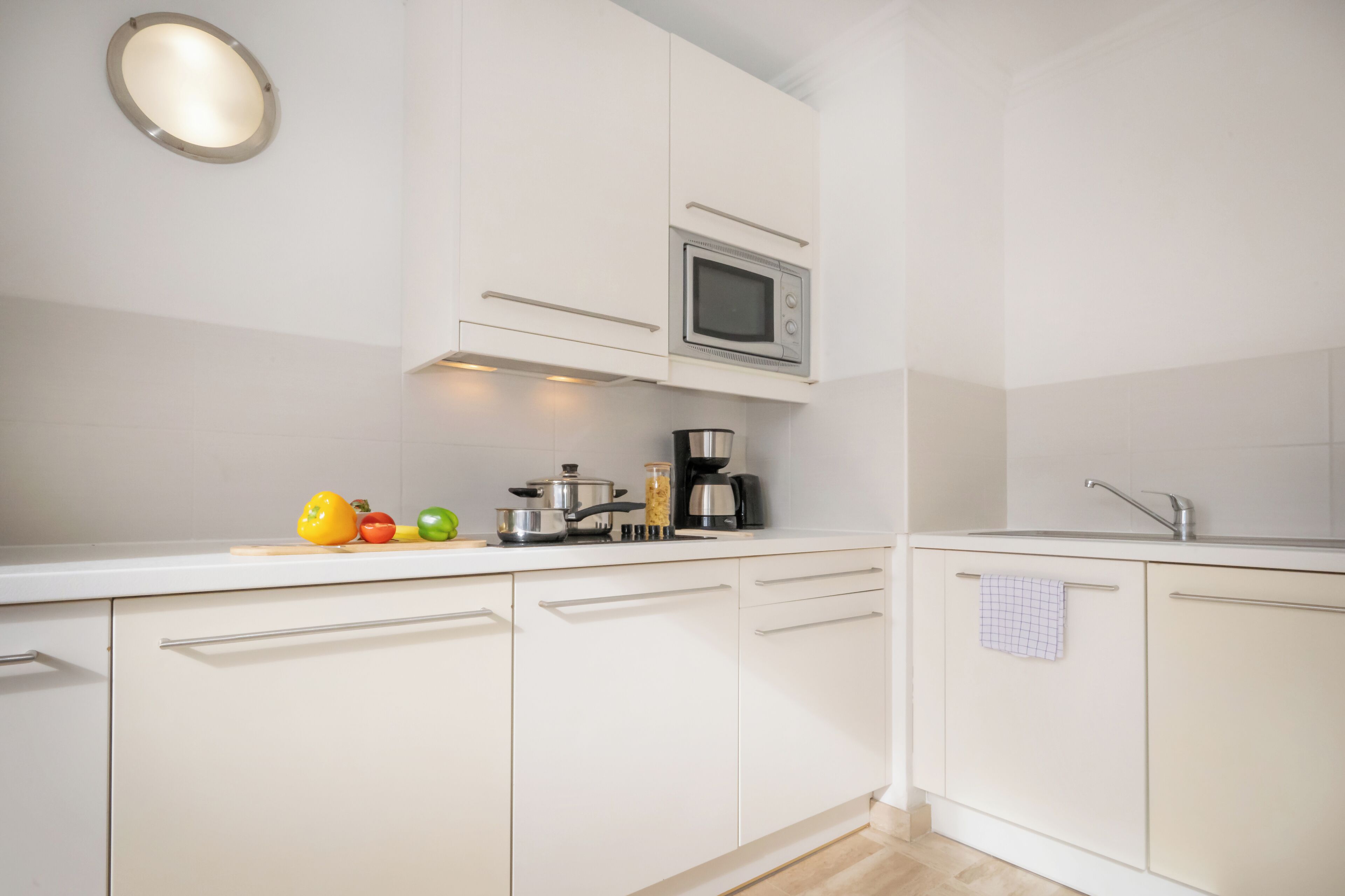 A modern kitchen with white cabinets, a microwave, a coffee maker, and fresh vegetables on the counter.