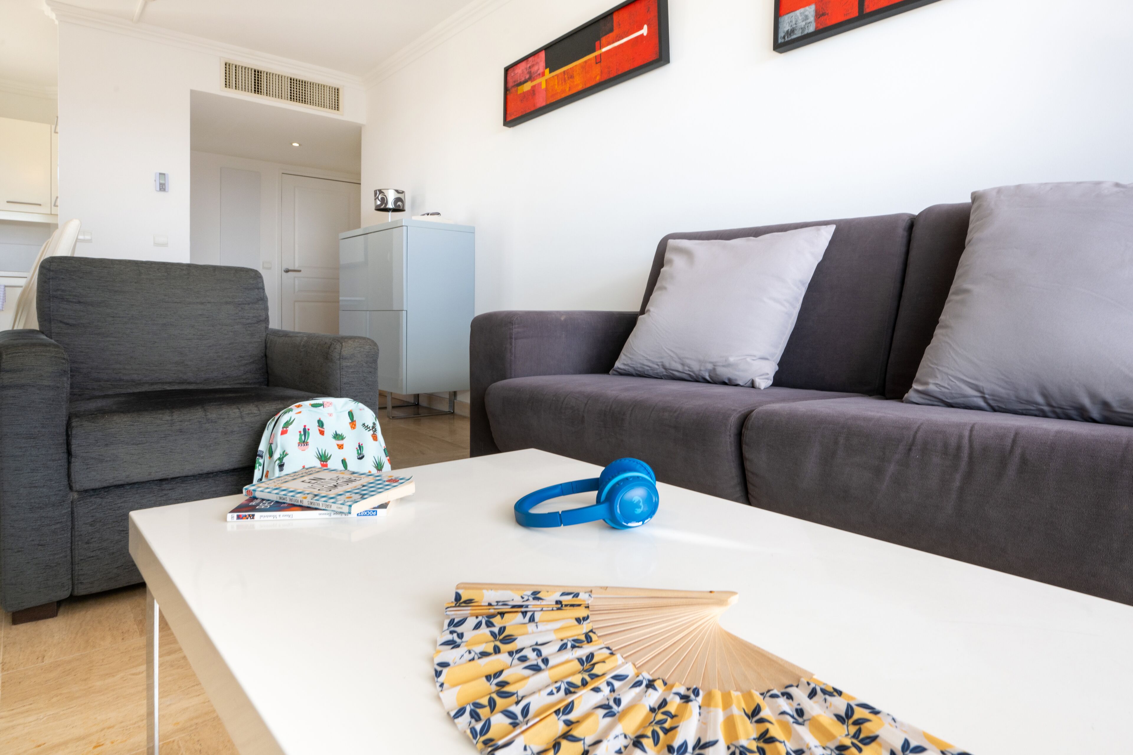 Un salón moderno con un sofá gris, una mesa de centro blanca y una mochila azul.
