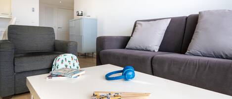 Un salón moderno con un sofá gris, una mesa de centro blanca y una mochila azul.