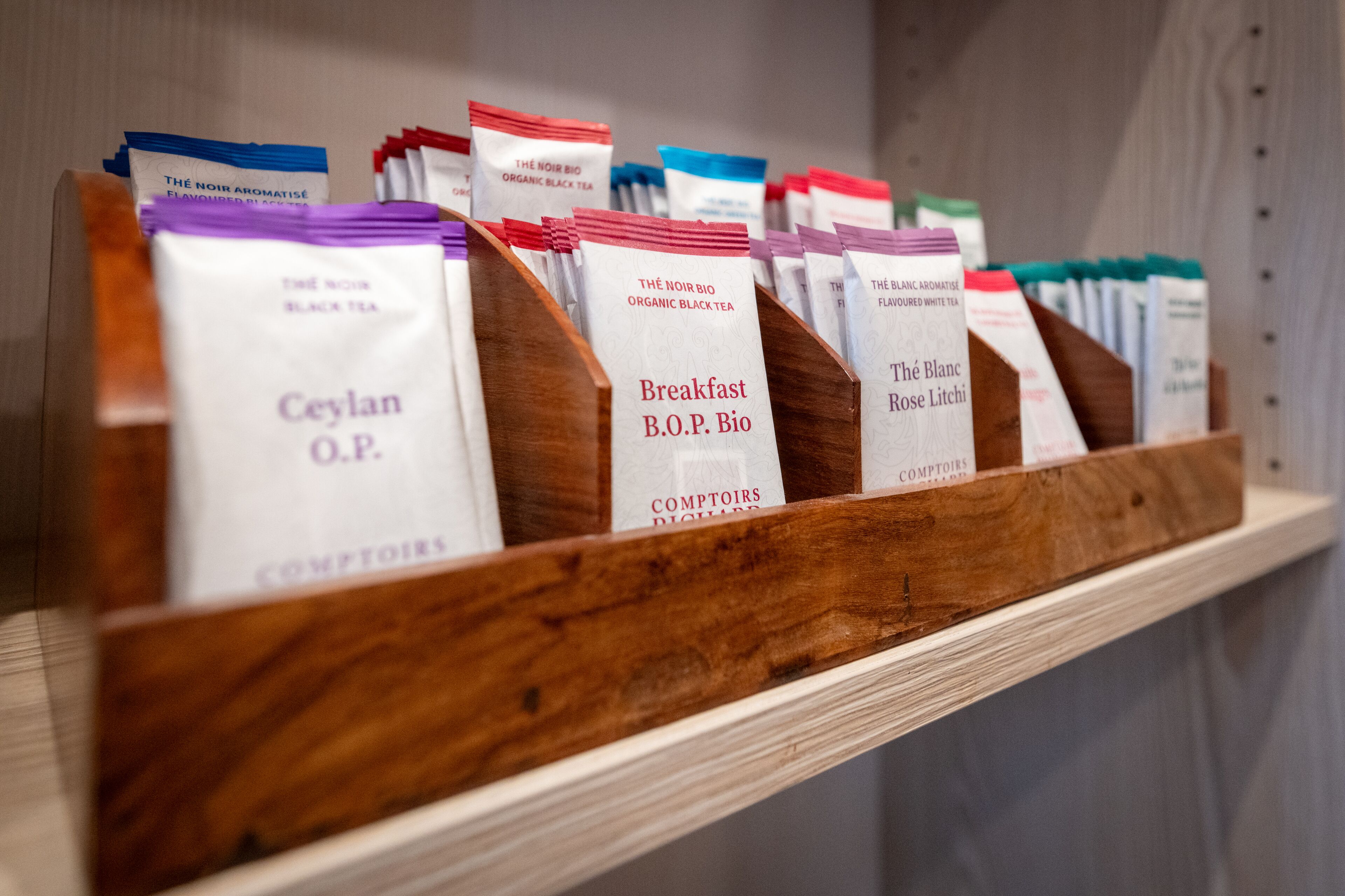 A wooden shelf with various tea packages labeled with names like "Ceylan O.P." and "Breakfast B.O.P. Bio".