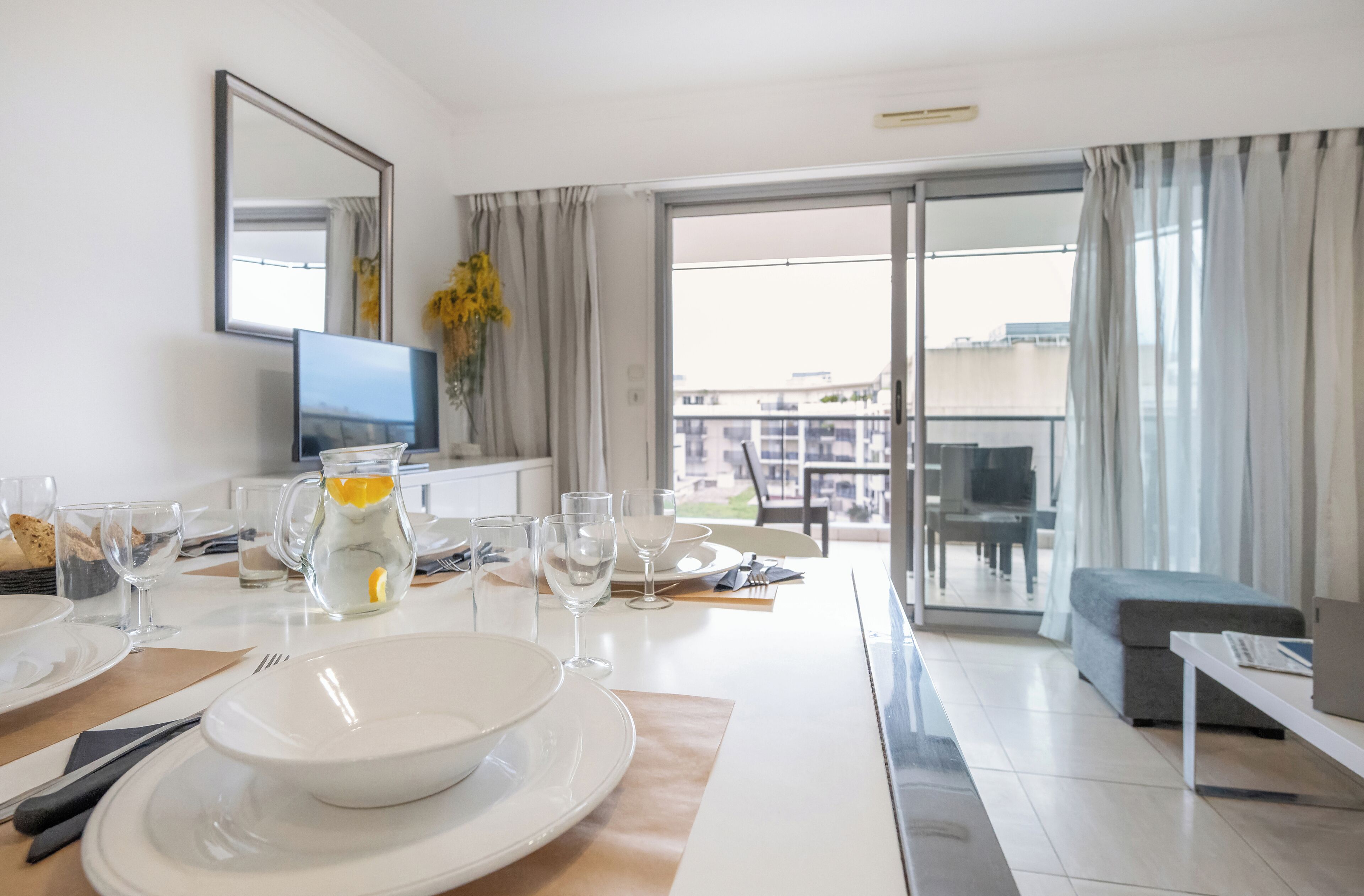 Una habitación de hotel moderna con comedor, televisor de pantalla plana y balcón con vistas a la ciudad.