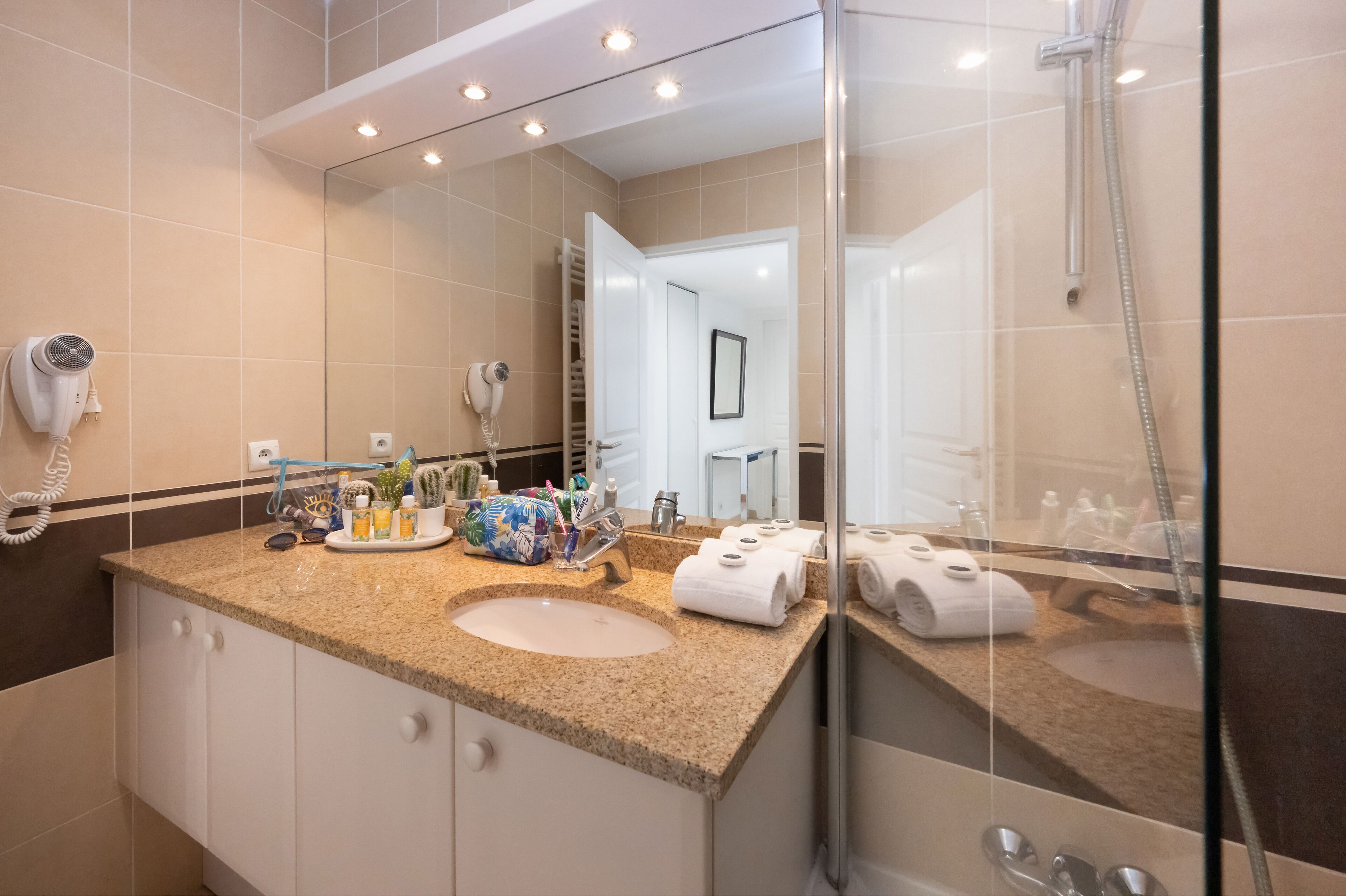 Un baño moderno con lavamanos de encimera de granito, un espejo grande, un cabezal de ducha de mano y un secador de pelo.