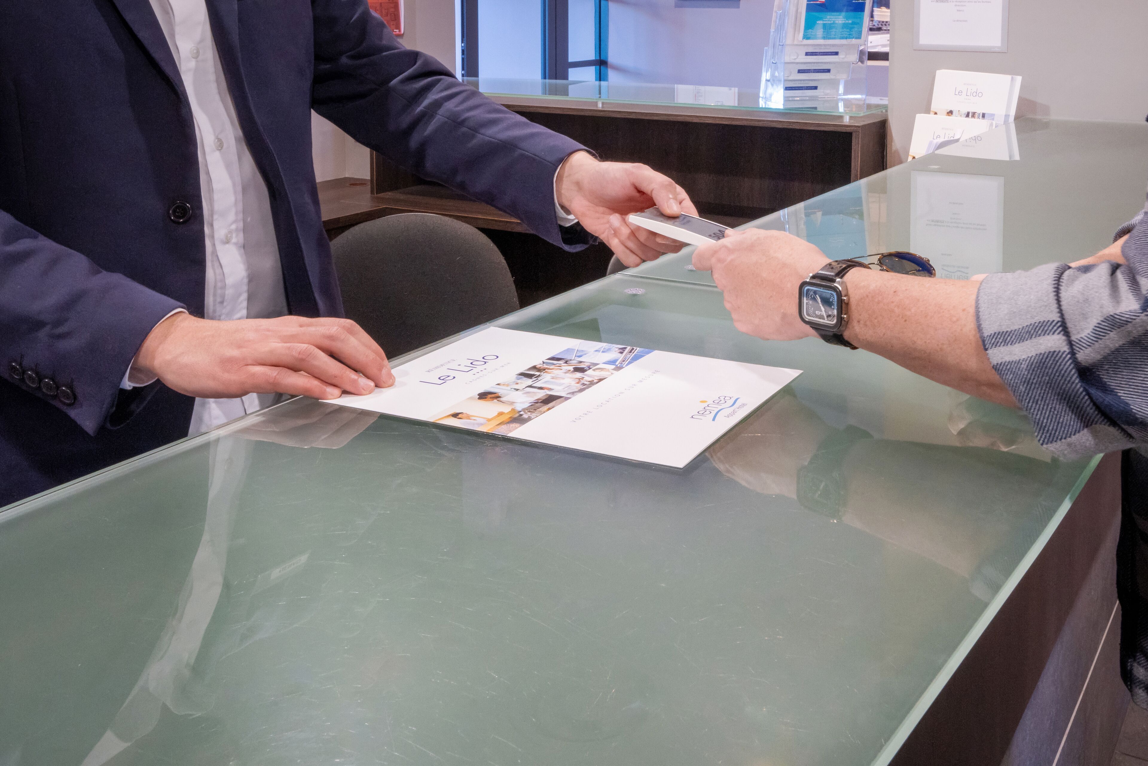 A person signing a document at a glass counter with a brochure on it.