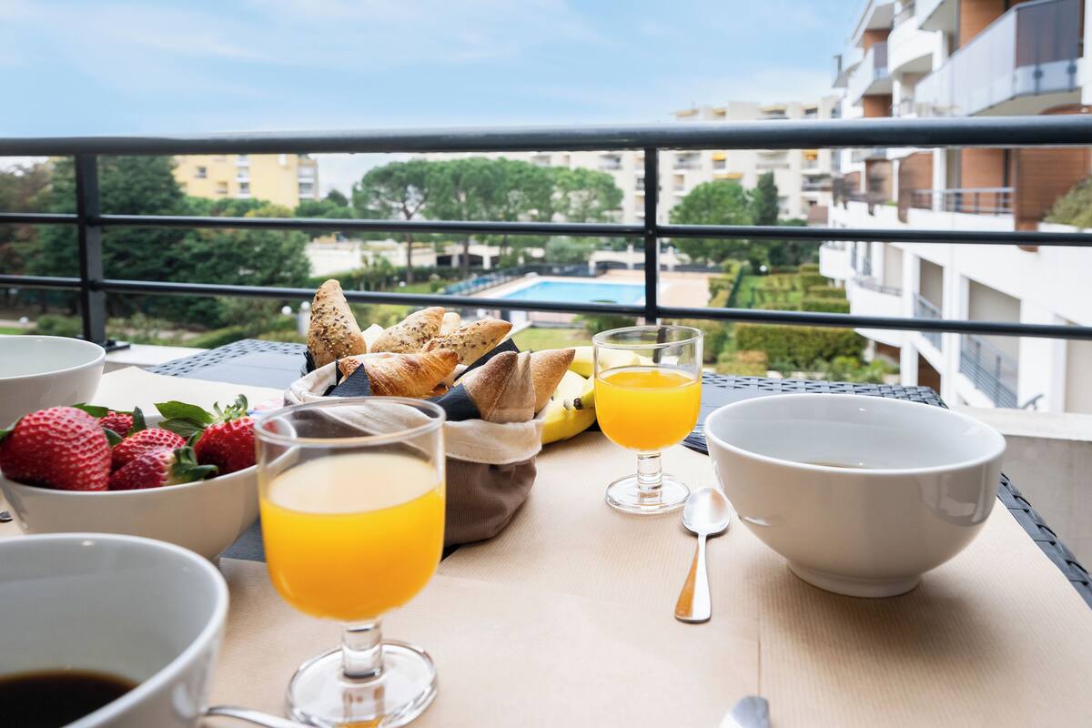 A breakfast setup on a balcony with a view of a swimming pool and buildings.