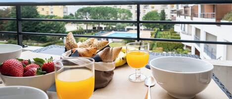 Un coin petit-déjeuner aménagé sur un balcon, avec vue sur une piscine et des immeubles.
