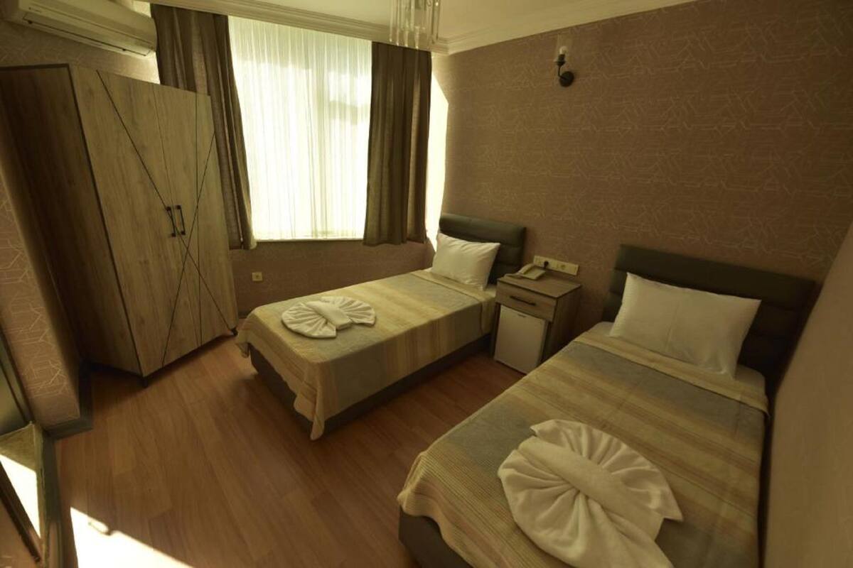 A hotel room with two beds, a wardrobe, a small desk, and a window with curtains.