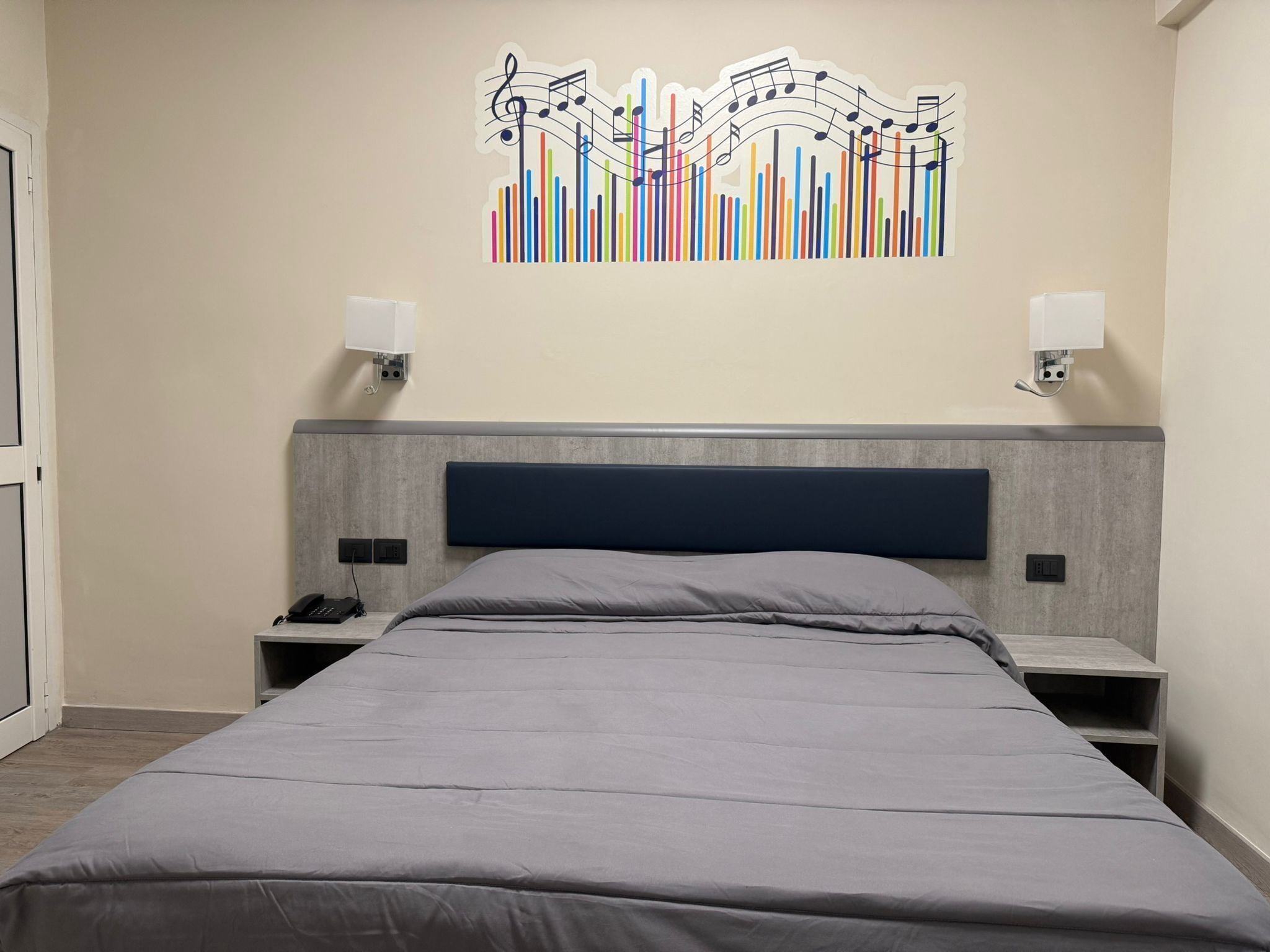 Una camera d'albergo moderna con un letto grande, una testiera con illuminazione integrata, comodini con lampade e un'opera d'arte astratta dai colori vivaci.