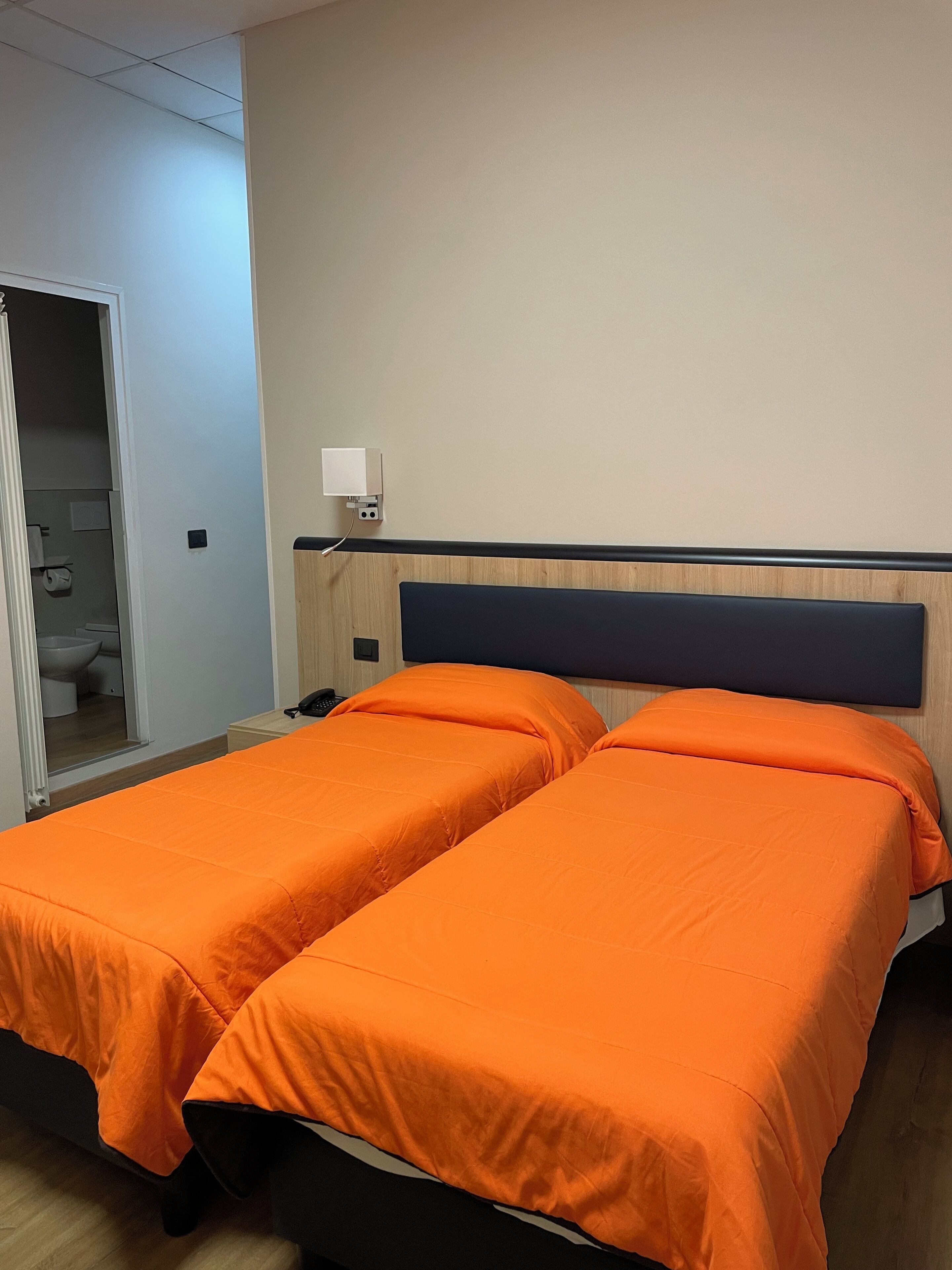 Habitación de hotel con dos camas individuales, cabecero de madera, mesita de noche y velador.