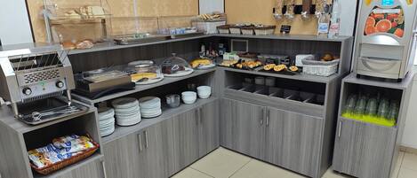 A self-service breakfast station with various food items, a coffee machine, and a beverage dispenser.