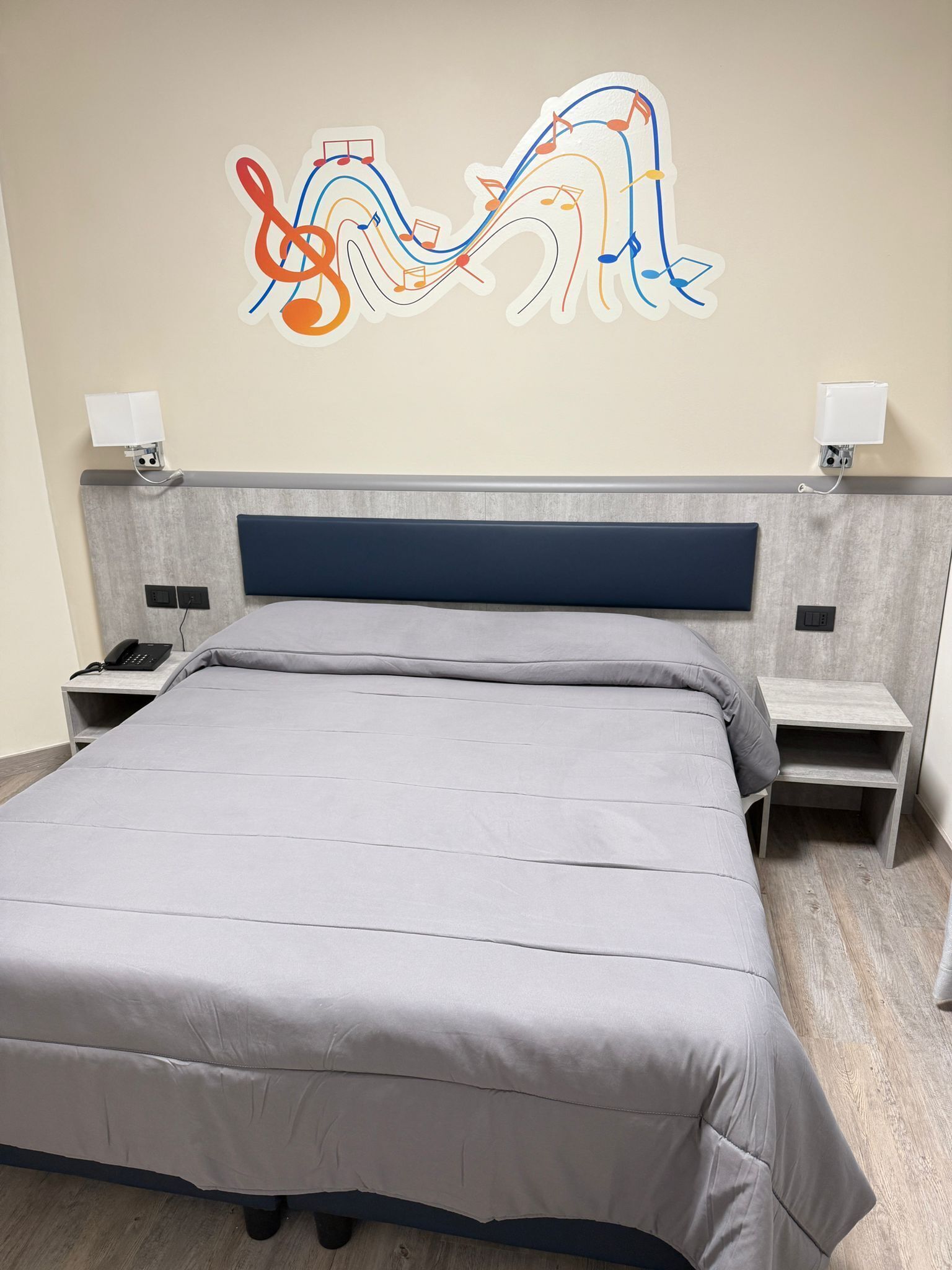 A modern bedroom with a large bed, a headboard with integrated lighting, bedside tables with lamps, and a wall art piece.