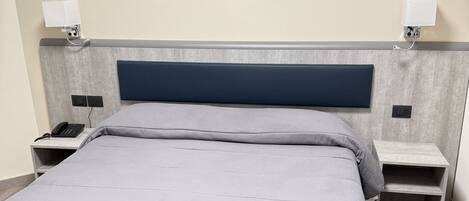A modern bedroom with a large bed, a headboard with integrated lighting, bedside tables with lamps, and a wall art piece.