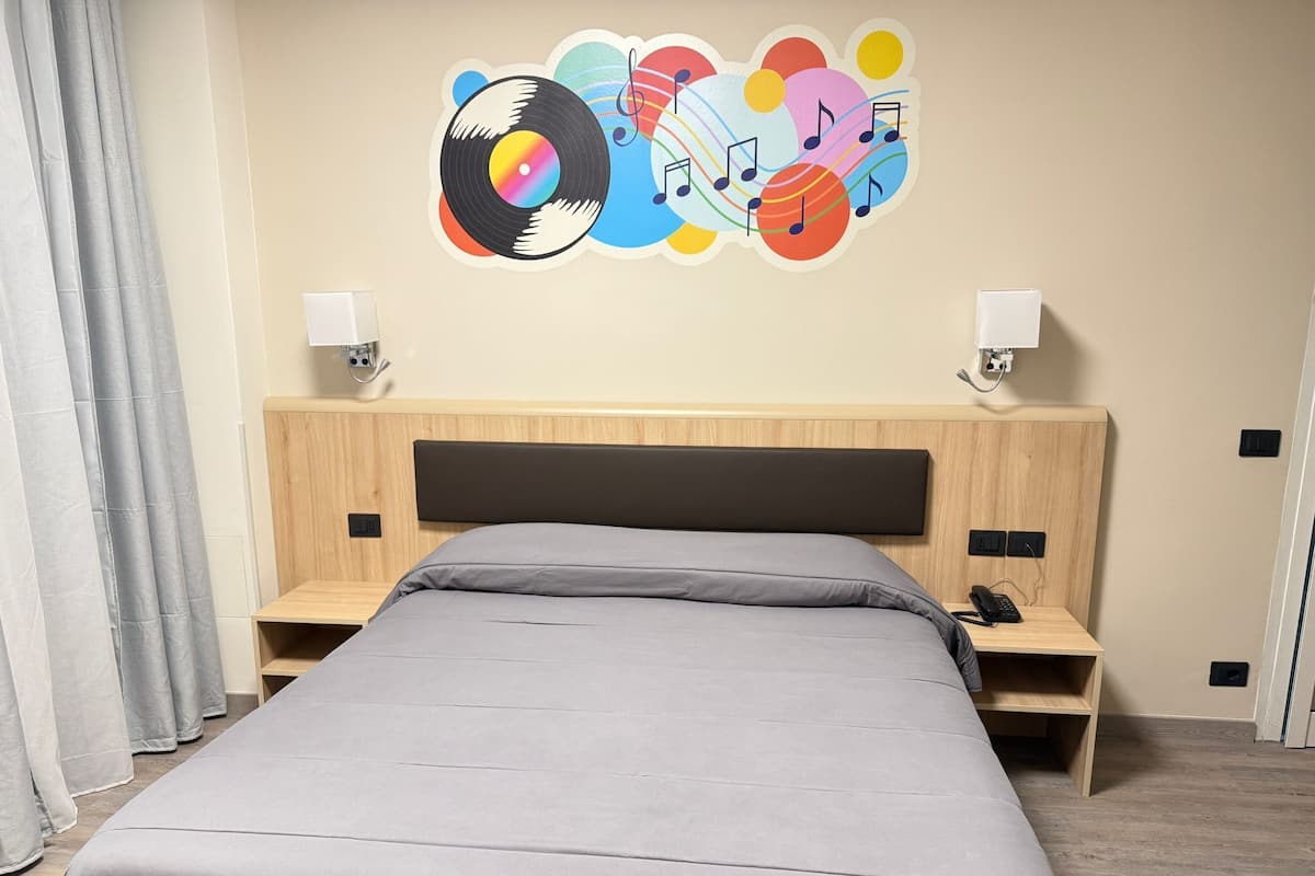 A modern hotel room with a large bed, two bedside tables, a headboard, and a wall decoration featuring a vinyl record and musical notes.