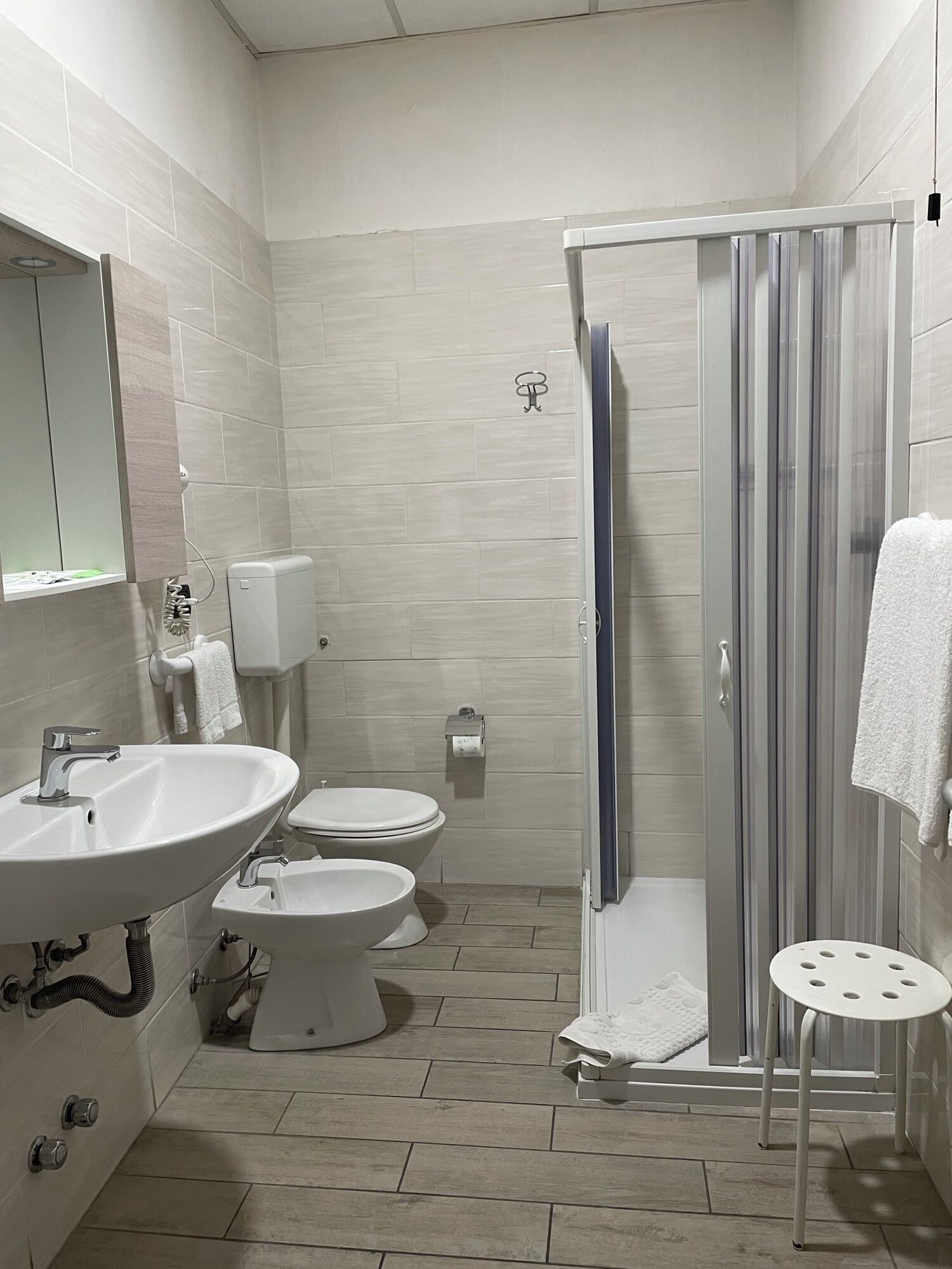 A bathroom with a sink, two toilets, a shower, and a towel rack.