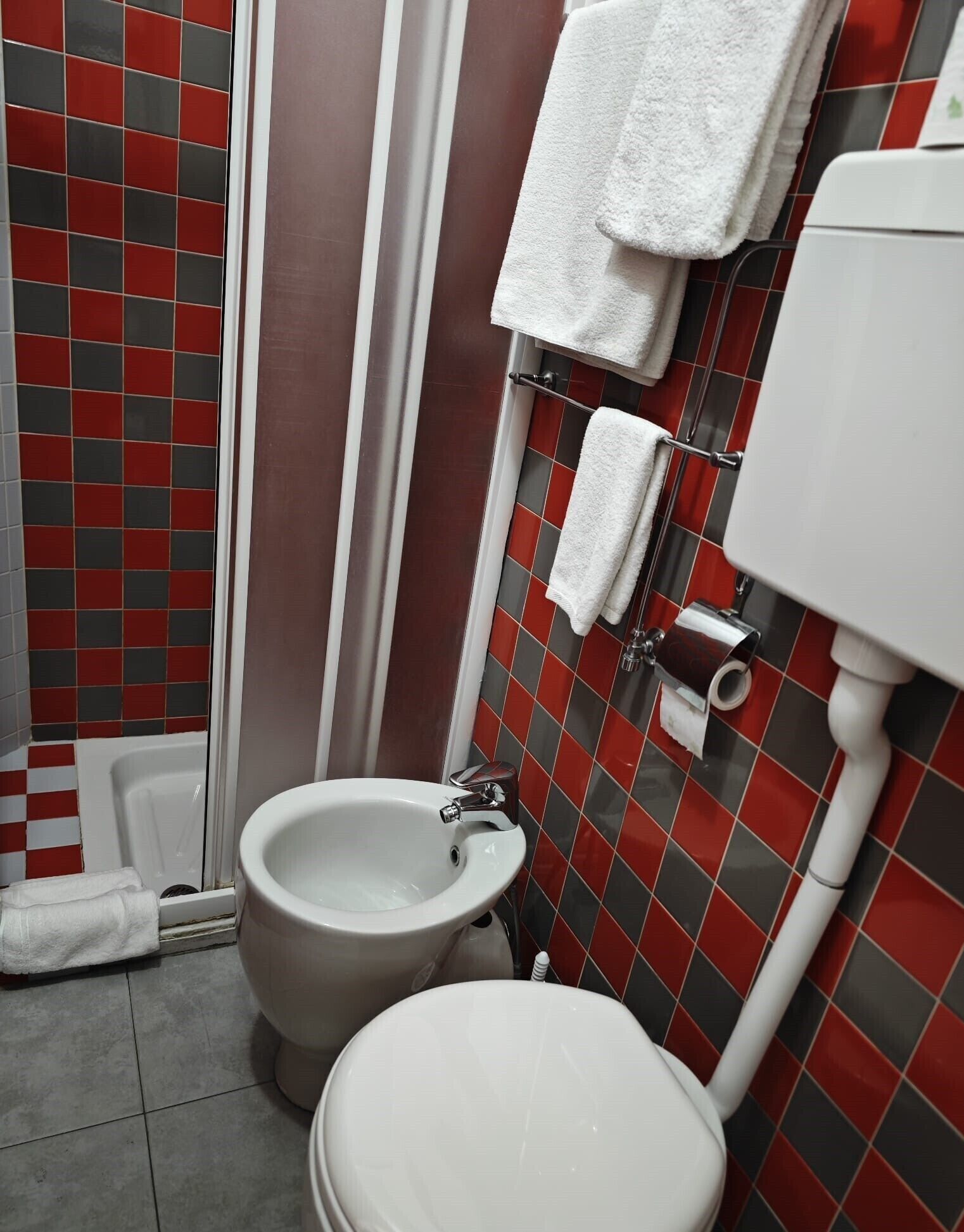 Une salle de bain équipée d’un bidet, de toilettes et de murs carrelés avec un motif à carreaux.