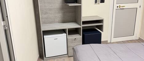 A compact bedroom with a bed, a wardrobe, a small desk, and a built-in microwave.