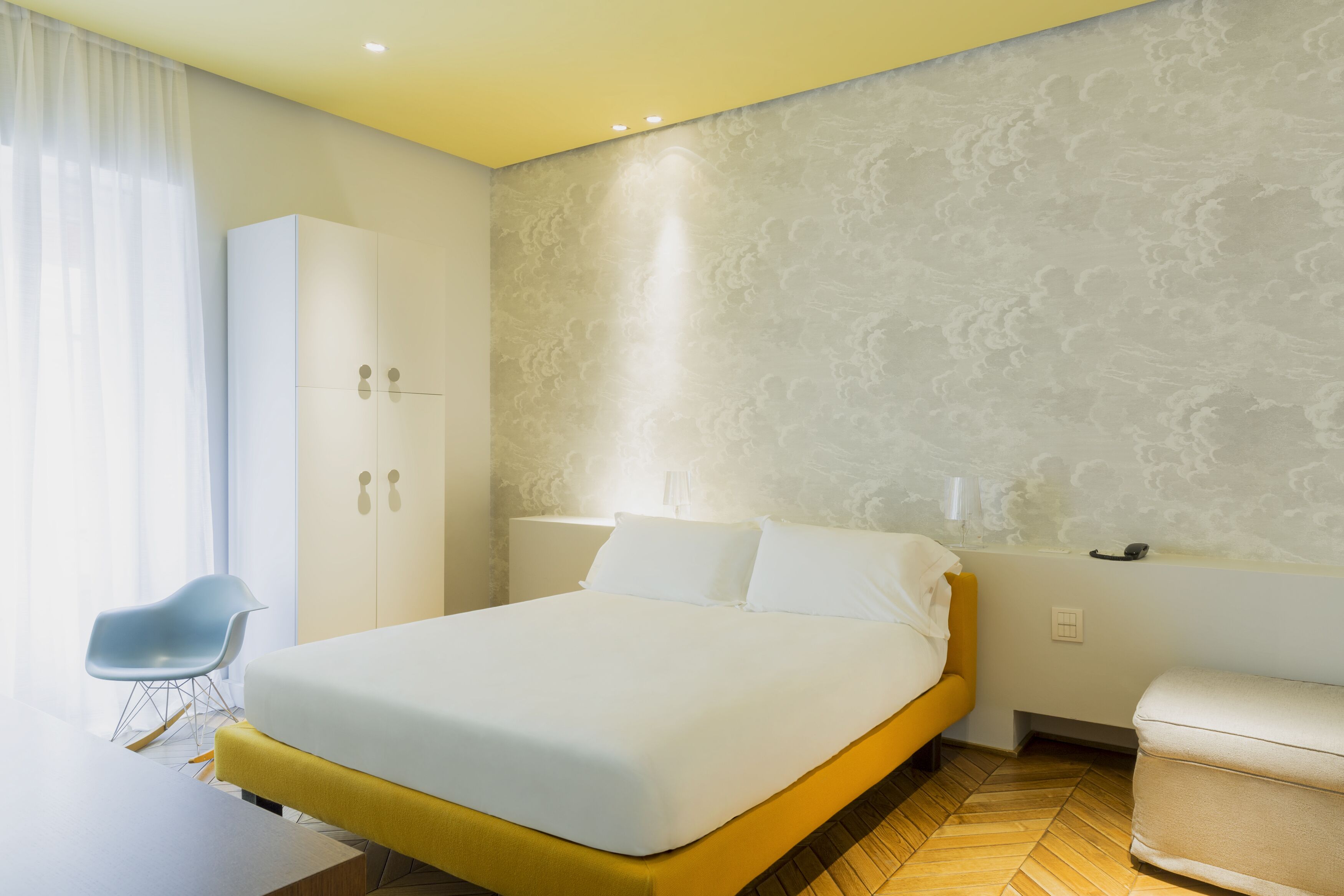 A modern hotel room with a large bed, a desk, a chair, and a wardrobe.