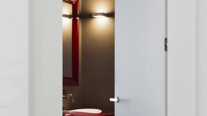 A narrow doorway leading to a bathroom with a red sink and a mirror above it. - Palazzo Segreti (Milan)
