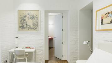 Una habitación con una cama, un escritorio con una silla, un cuadro en la pared y una puerta que da a otra habitación.