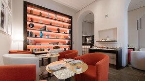 A modern interior with a central table, orange chairs, a bookshelf, and a kitchen area. - Palazzo Segreti (Milan)