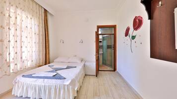 Un dormitorio con una cama, una mesita de noche pequeña y blanca, un espejo y una puerta que da a un baño.