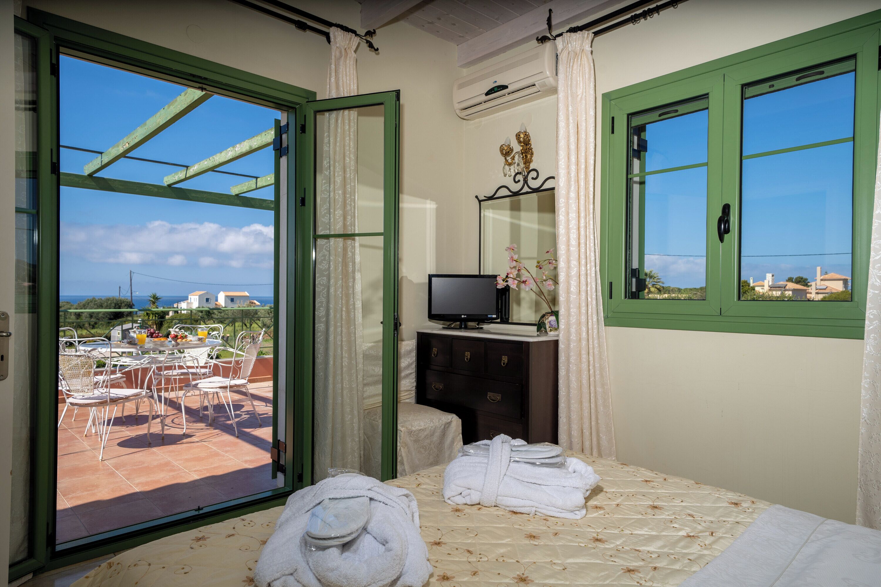 A bedroom with a bed, a television, a dresser, and a view of the terrace.