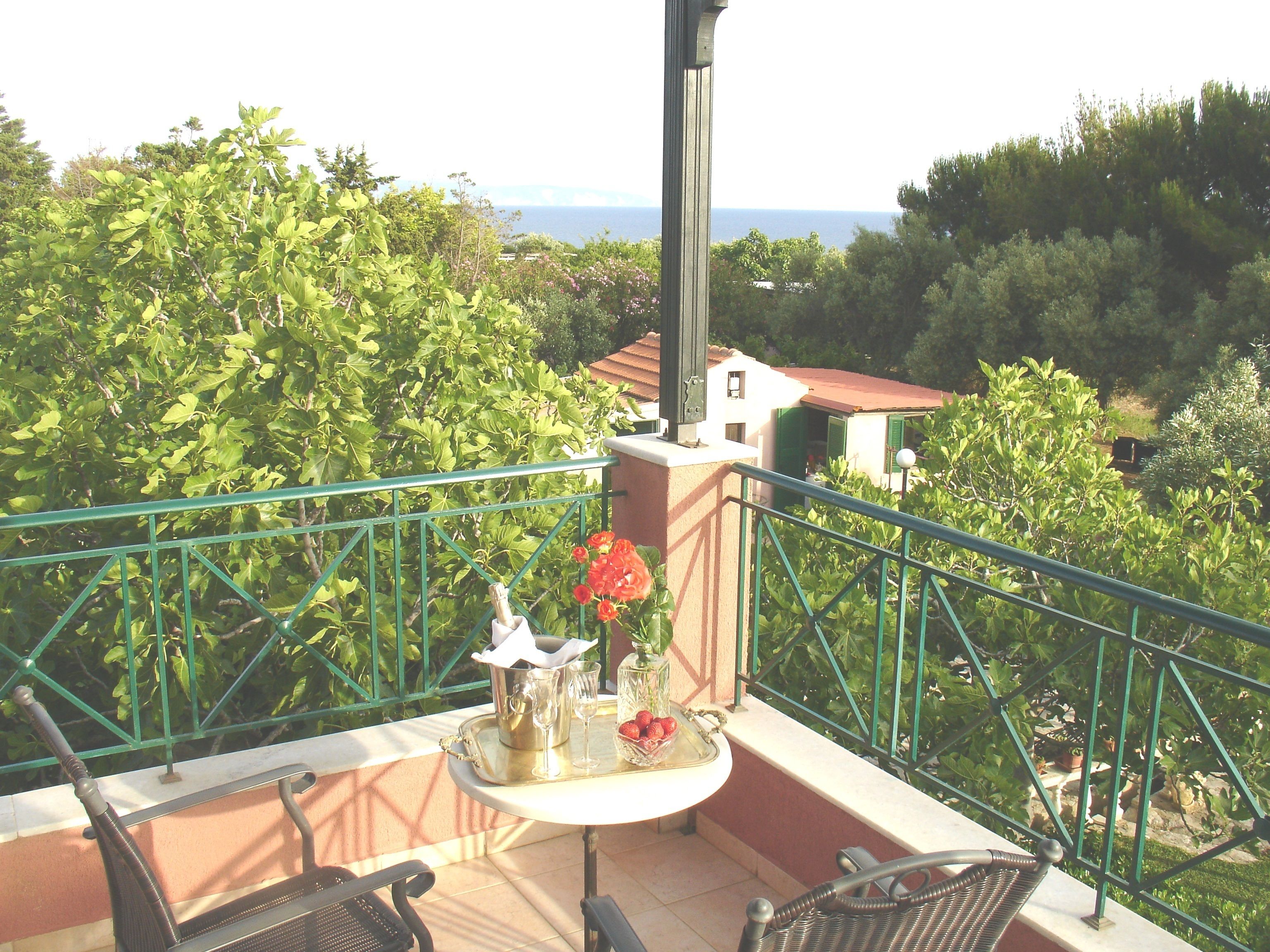 A balcony with a table set for two, featuring a bottle, glasses, and a fruit bowl.