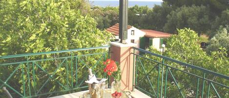 A balcony with a table set for two, featuring a bottle, glasses, and a fruit bowl.