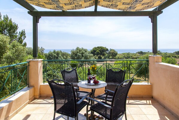 A covered outdoor seating area with a table and chairs, overlooking a scenic landscape. - Monambeles Villas (Kefalonia)