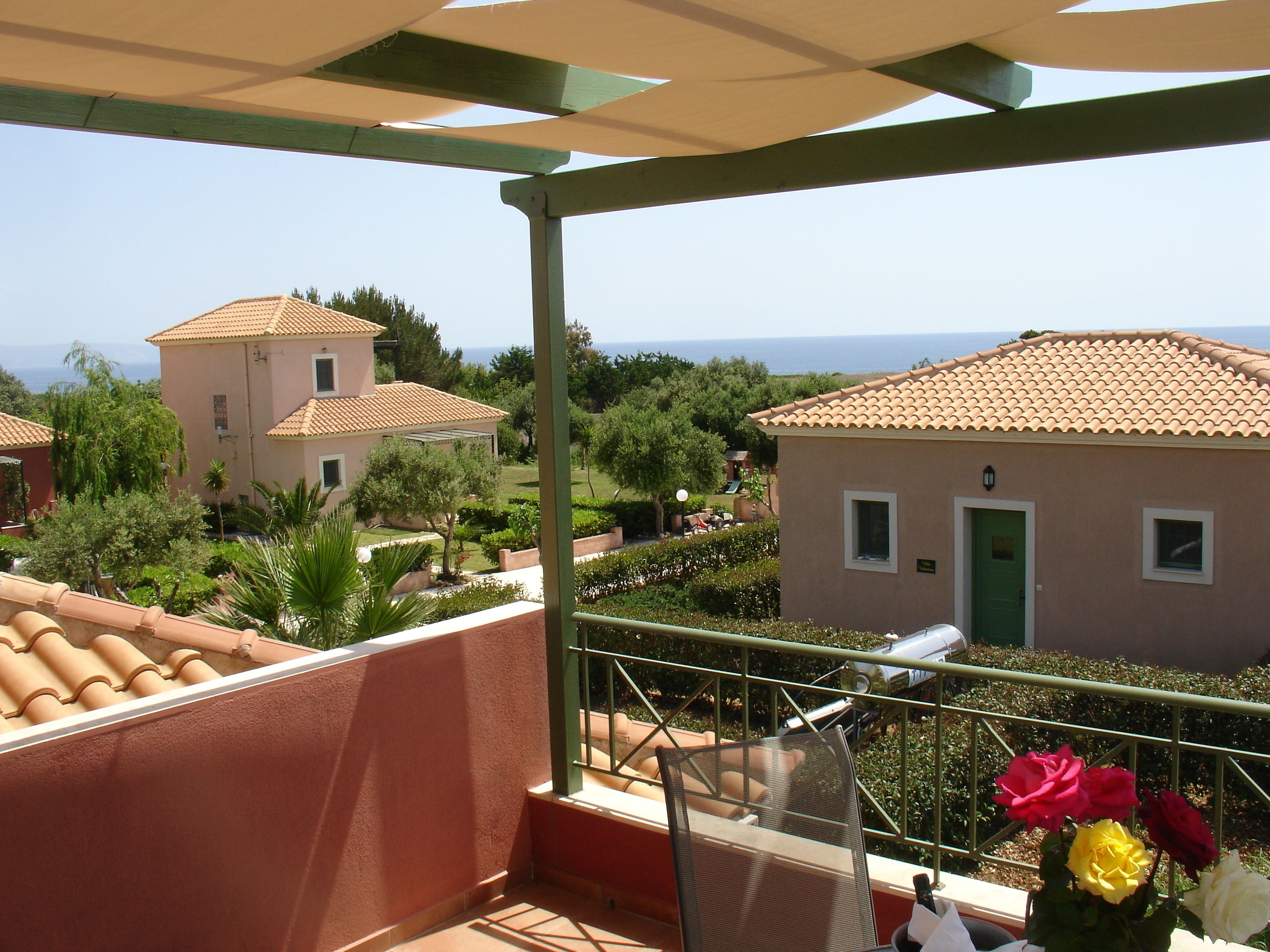 A balcony with a view of a villa, a pergola, and a garden.