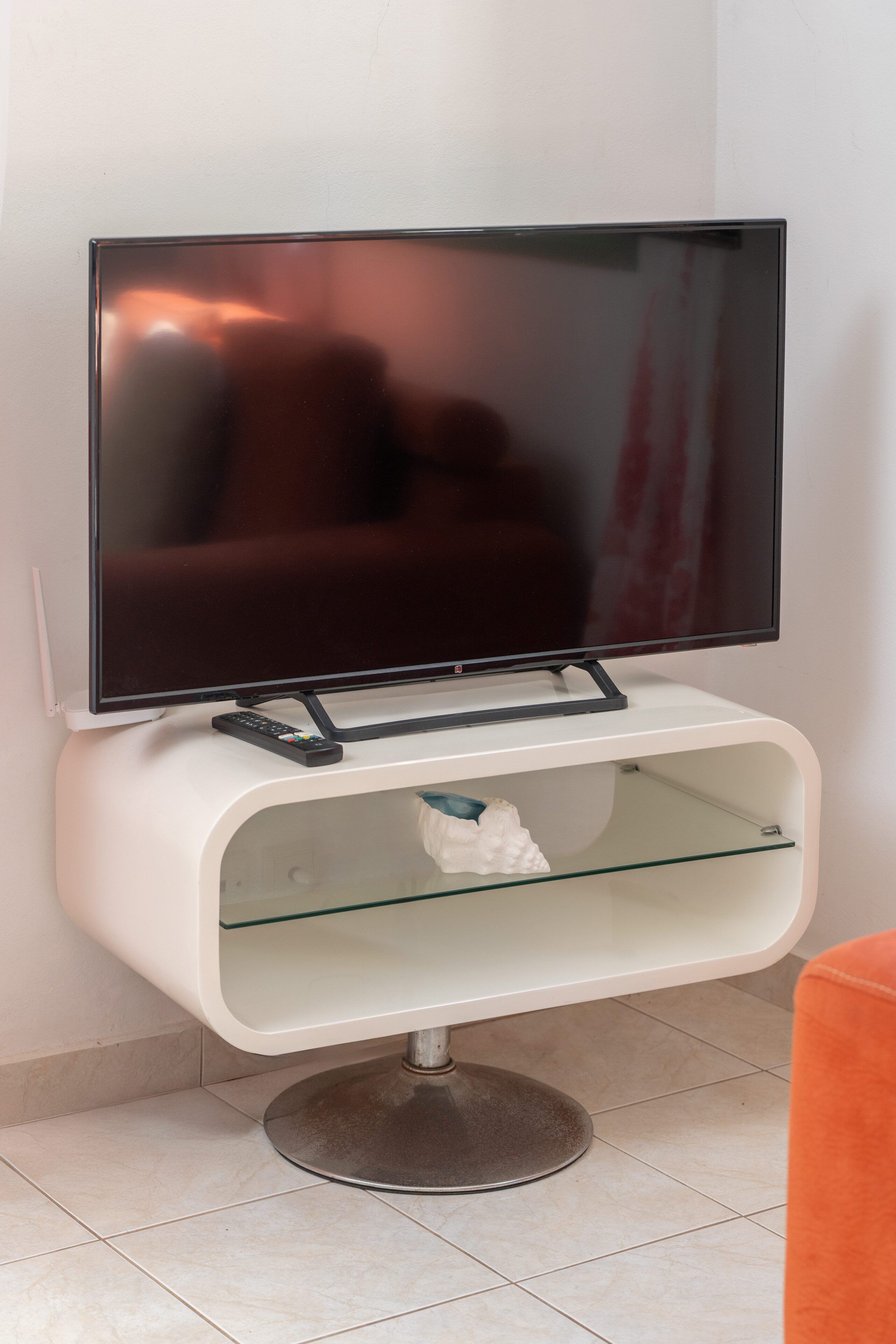 Un televisor de pantalla plana sobre un soporte blanco con un estante de vidrio debajo.